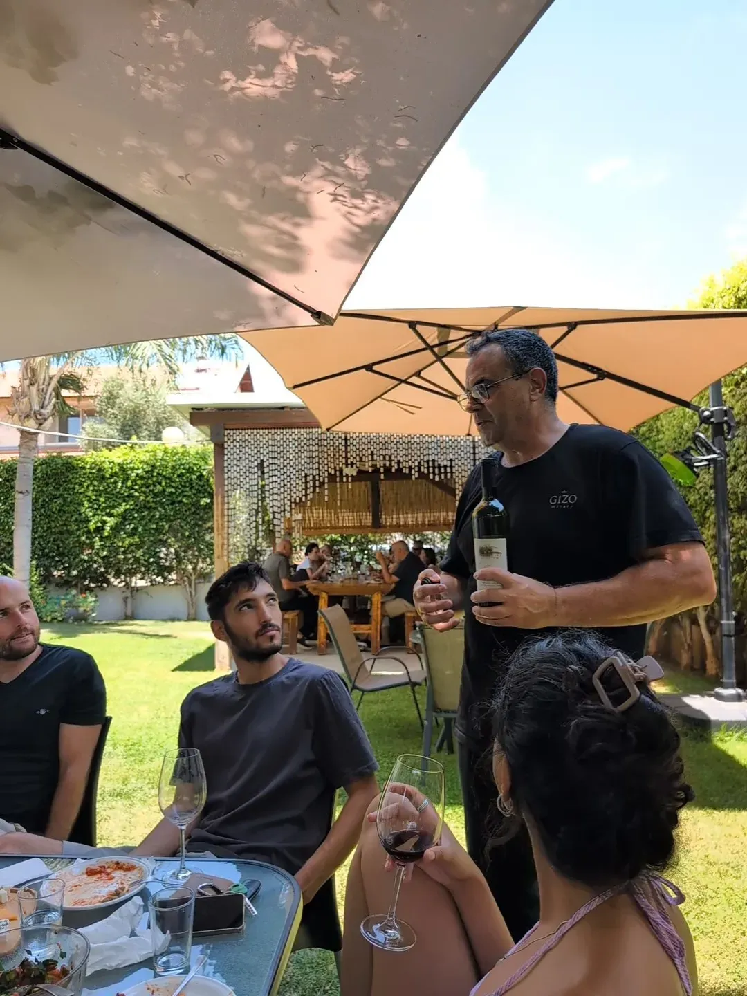 יואב מציג בקבוק ומסביר על היין לאורחים בחצר היקב